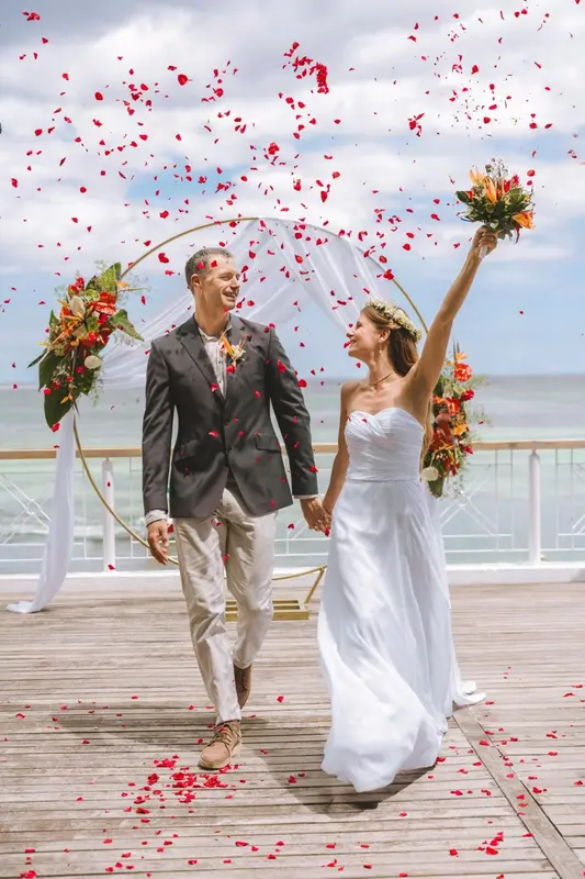 Un couple souriant se tient la main sur une terrasse décorée de fleurs et de pétales.