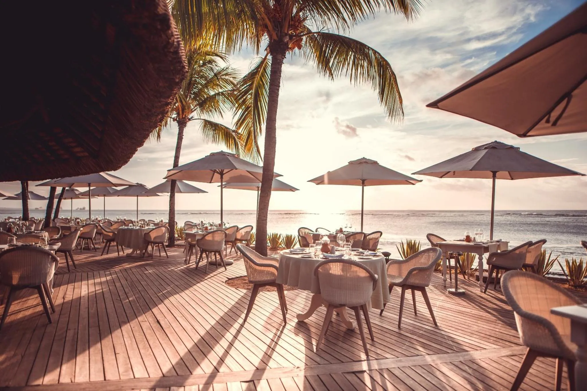 Tables dressées sur une terrasse en bois face à la mer au coucher du soleil.