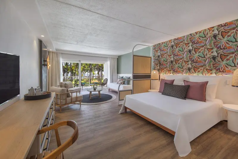 Une chambre lumineuse avec un grand lit et un coin salon donnant sur une vue extérieure.