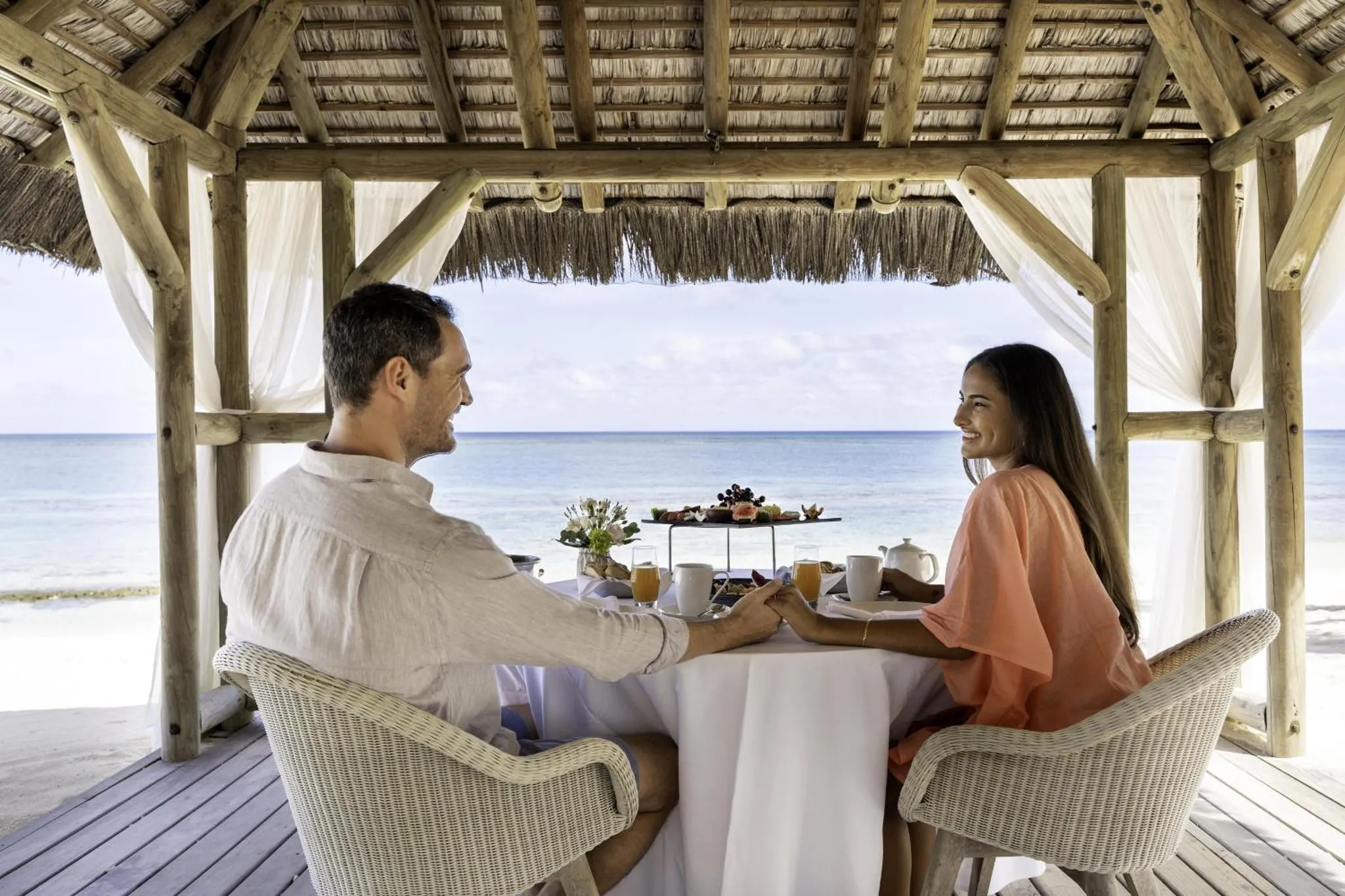 Un couple prend son petit-déjeuner à une table en plein air face à la mer.