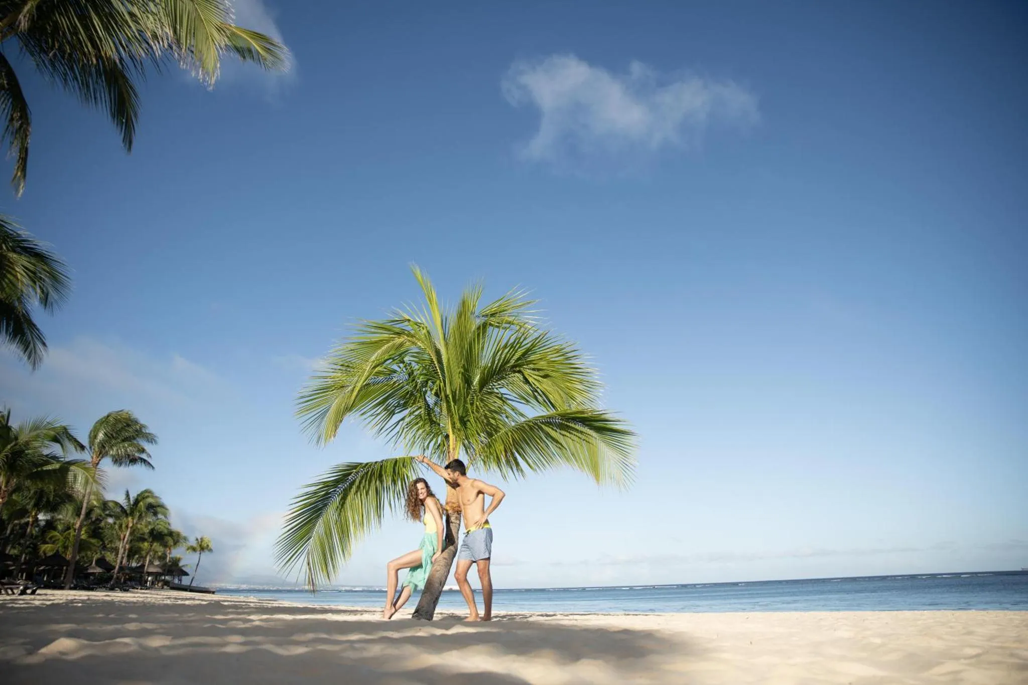 Un couple se tient sur une plage de sable blanc sous des palmiers.