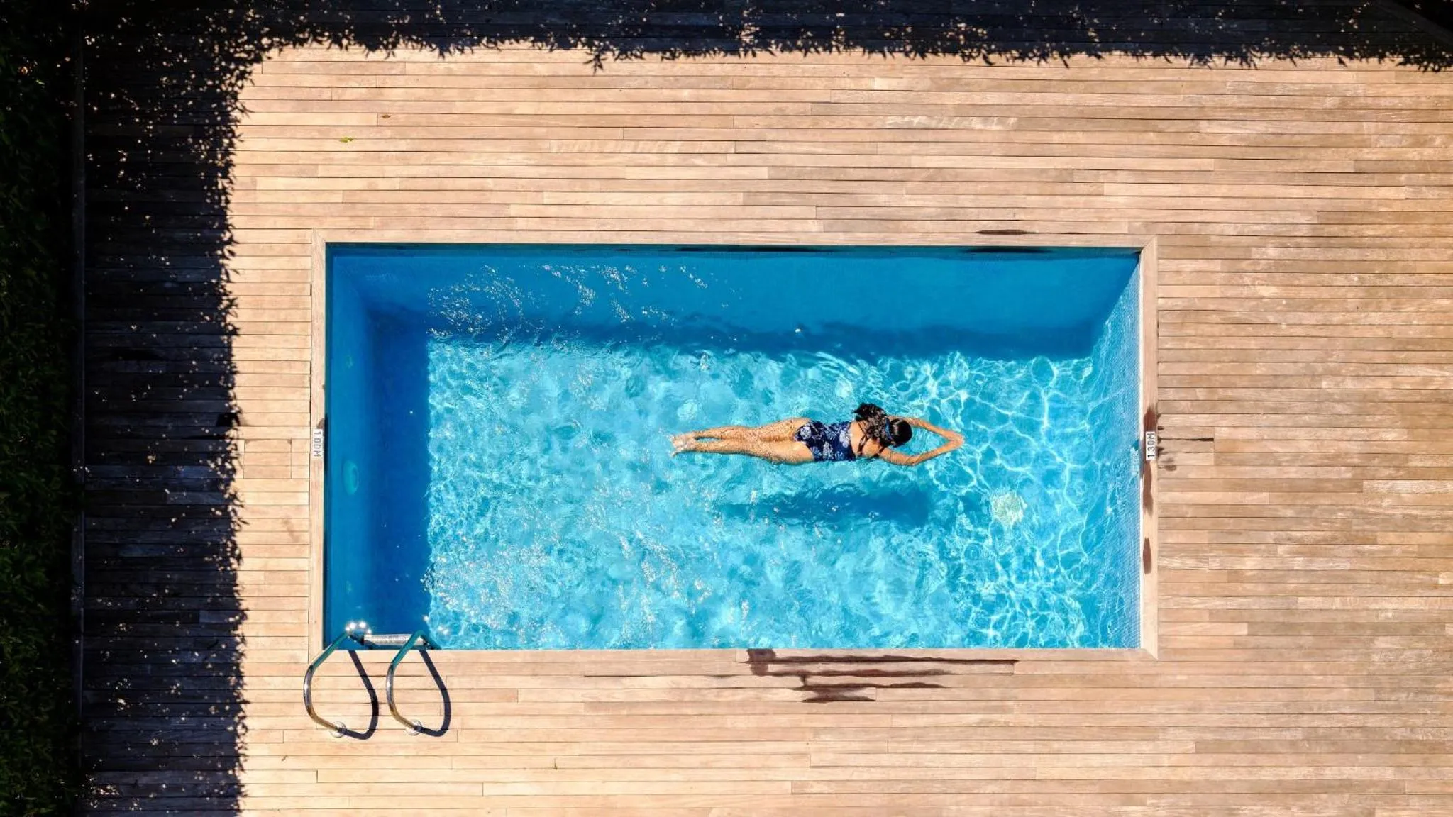 Une personne se détend dans une piscine rectangulaire entourée d'une terrasse en bois.