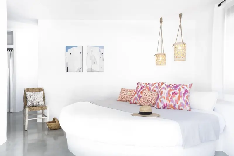 Une chambre lumineuse avec un grand lit blanc et des coussins colorés.