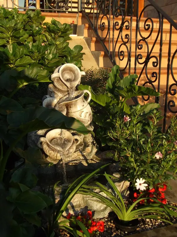 Une fontaine en pierre orne un jardin luxuriant avec des plantes et des fleurs.