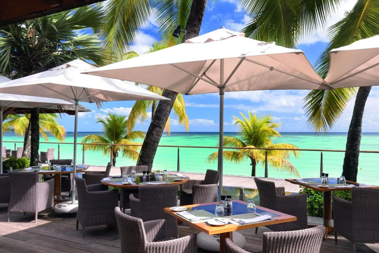 Terrasse ombragée avec tables et chaises face à la mer turquoise.