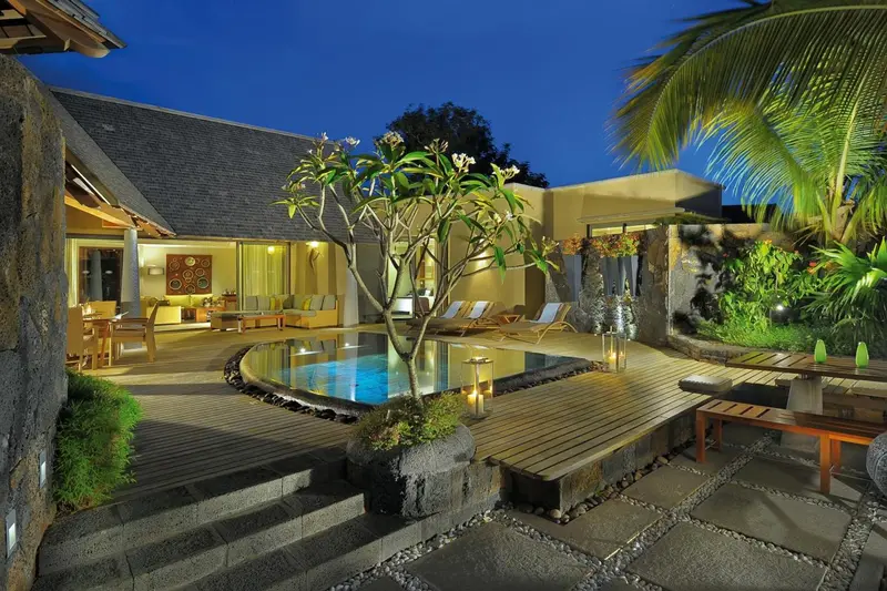 Une petite piscine est entourée d'une terrasse en bois et de végétation tropicale.
