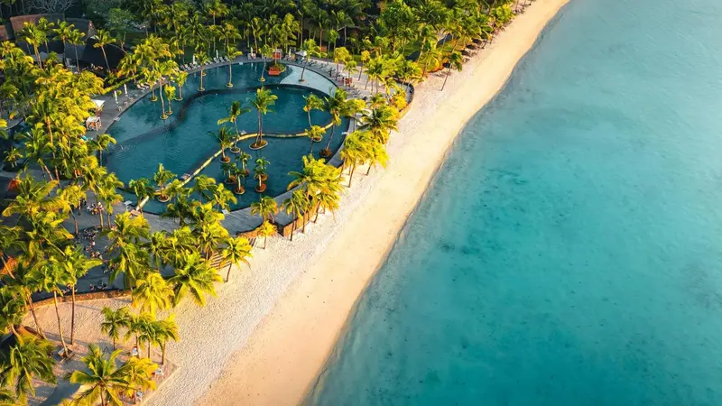 Vue aérienne d'une plage de sable blanc bordée de palmiers et d'une piscine.
