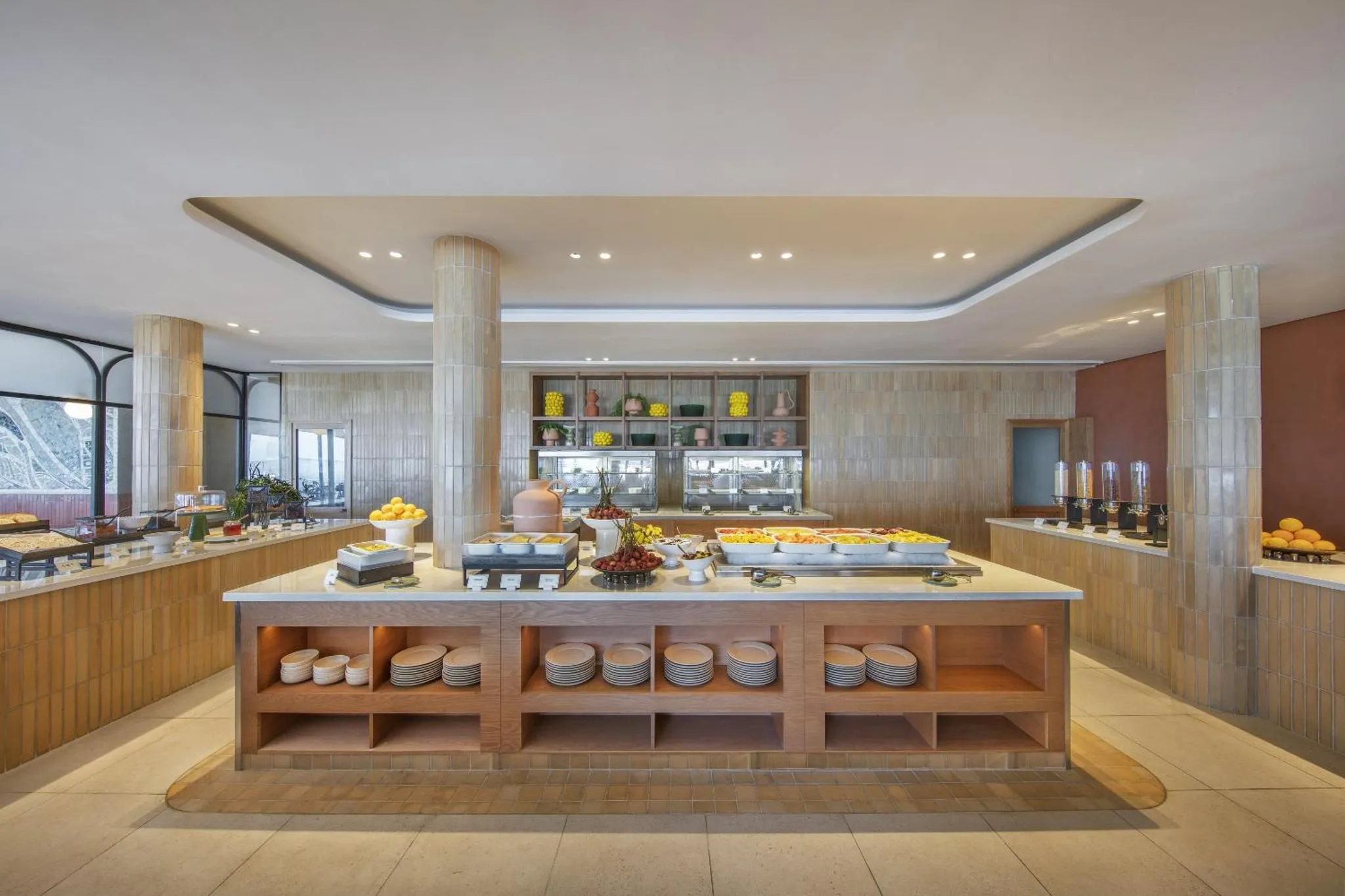 Un buffet propose une grande variété de plats et de fruits frais dans une salle lumineuse.