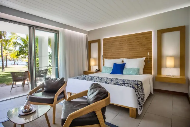 Une chambre lumineuse avec un grand lit et un coin salon donnant sur une terrasse.