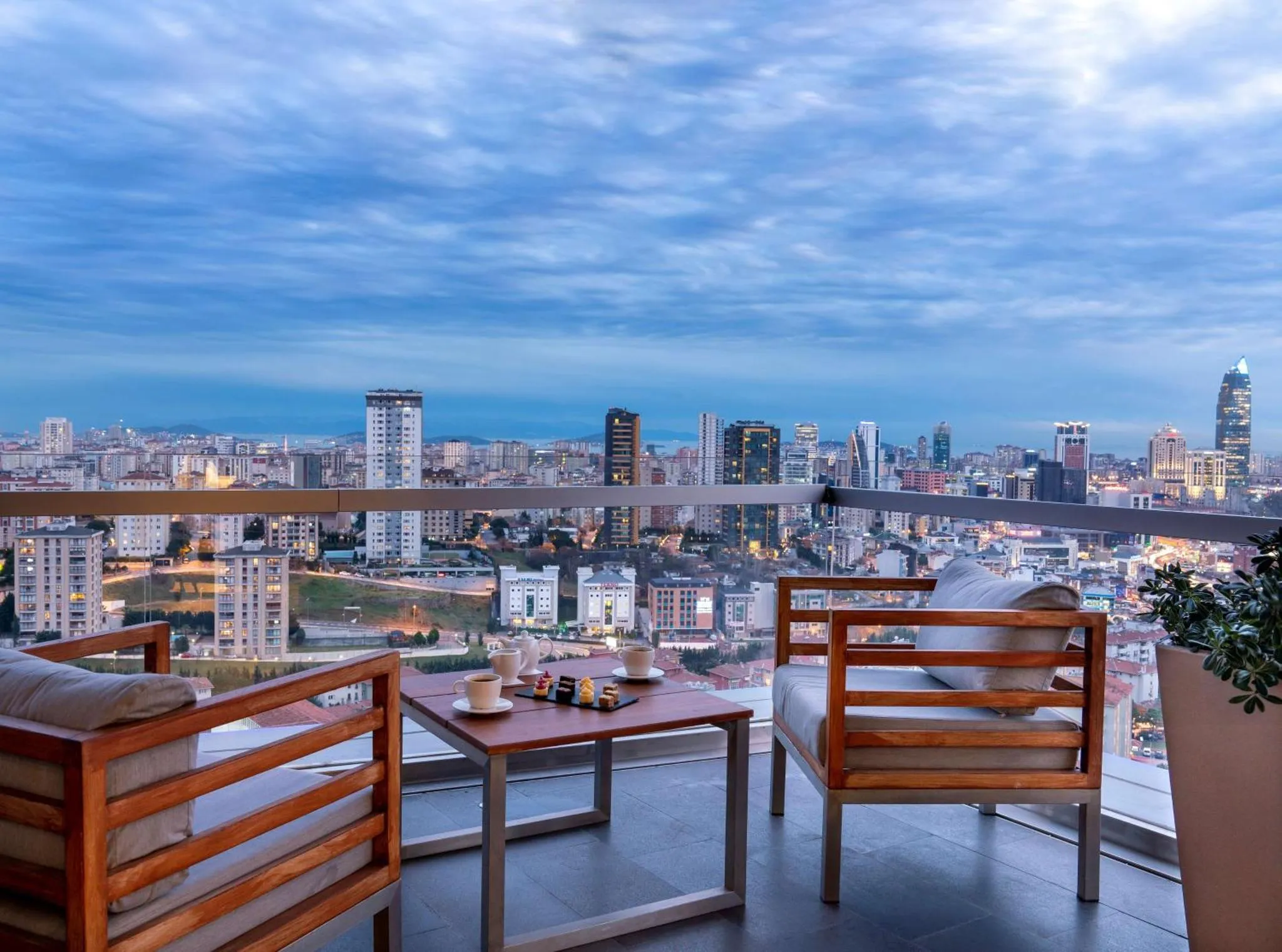 Terrasse avec mobilier en bois donnant sur une ville illuminée au crépuscule.