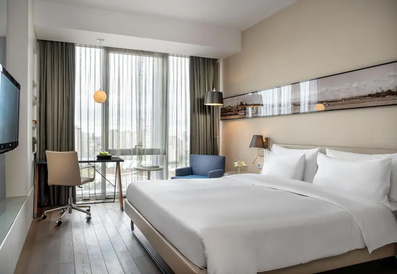 Une chambre lumineuse avec un grand lit et un bureau près de la fenêtre.