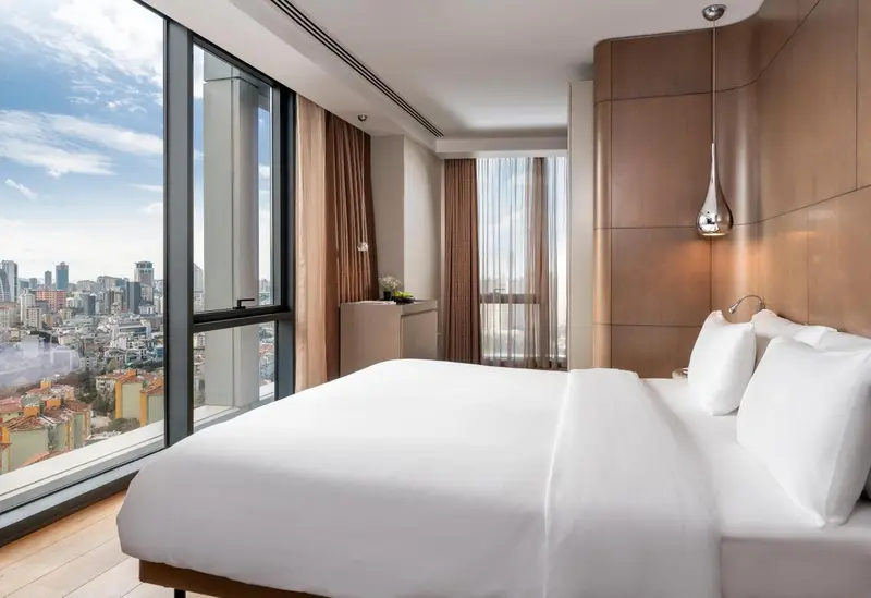 Chambre lumineuse avec un grand lit et une vue sur la ville.