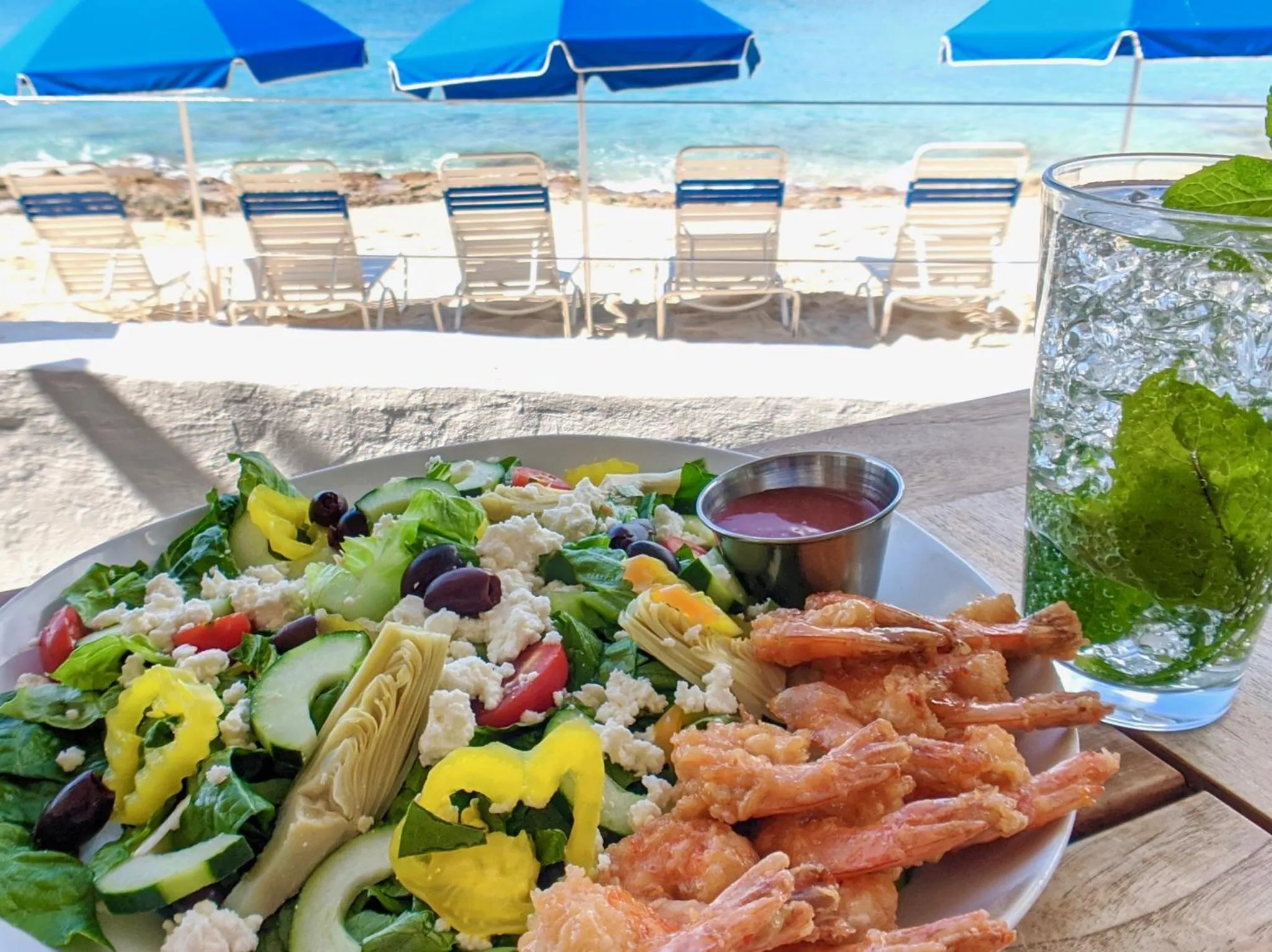 Une salade colorée et une boisson fraîche sont présentées sur une table en bord de mer.