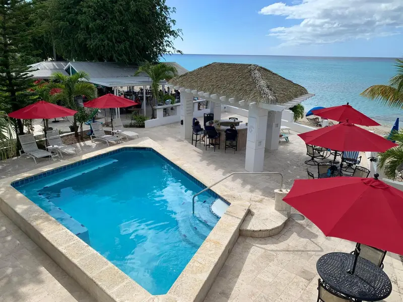 Une piscine turquoise bordée de chaises longues rouges et de parasols, avec un bar en fond.