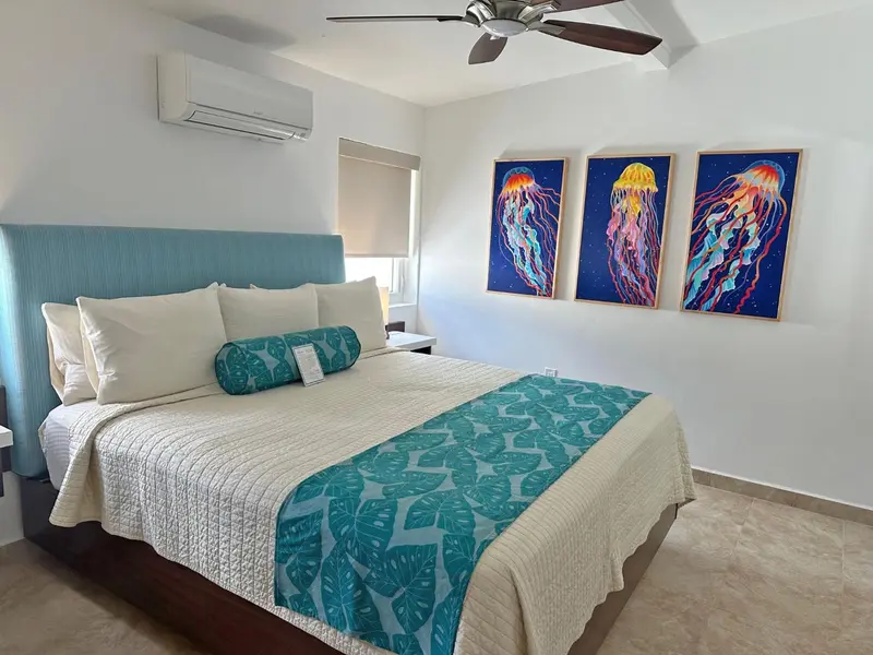 Une chambre lumineuse avec un grand lit recouvert d'une courtepointe blanche et turquoise.