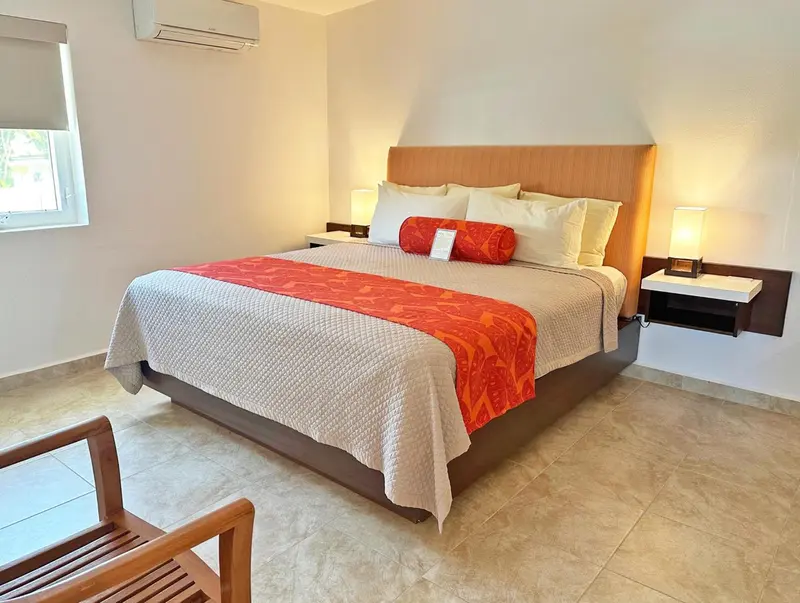 Une chambre lumineuse avec un grand lit recouvert d'une courtepointe blanche et d'un jeté rouge.