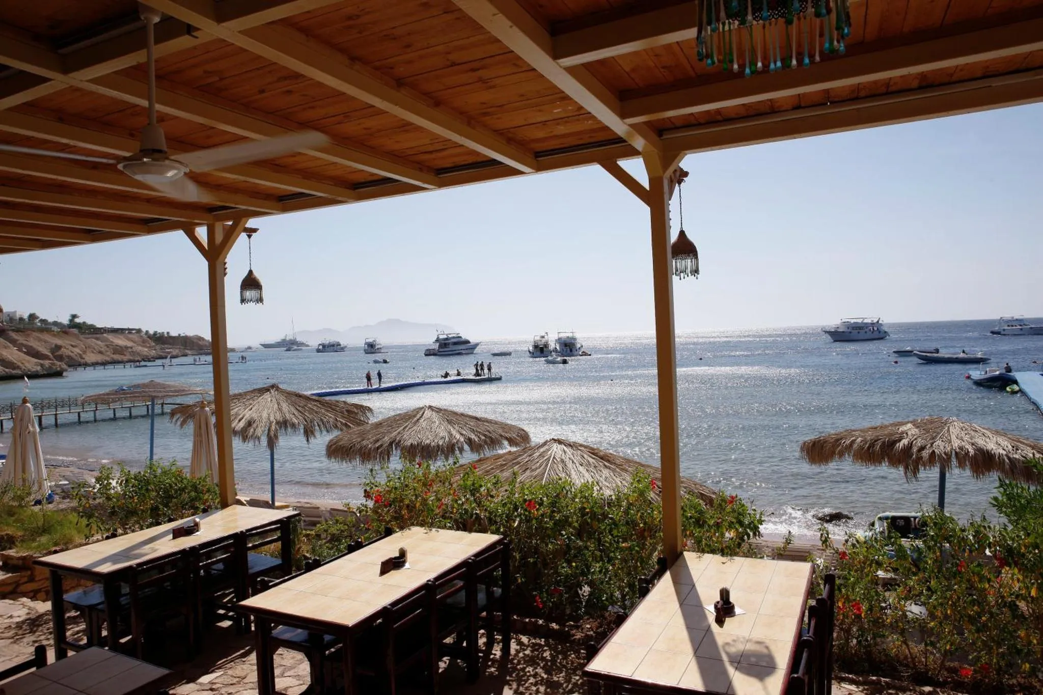 Terrasse ombragée donnant sur la mer et une plage de sable.