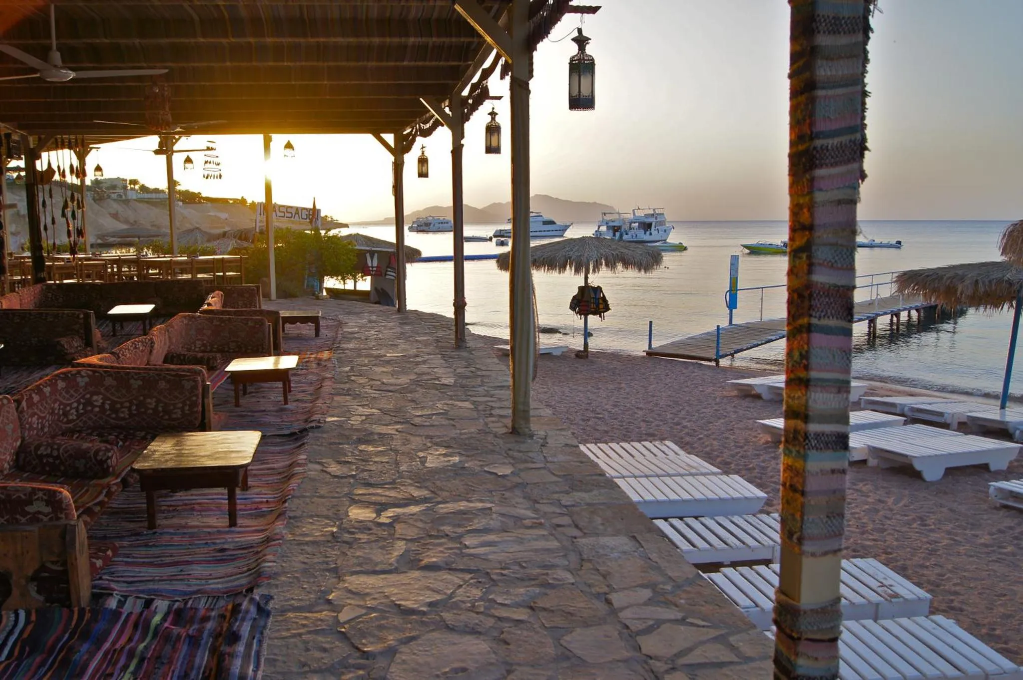 Terrasse ombragée avec mobilier de détente face à la mer au coucher du soleil.