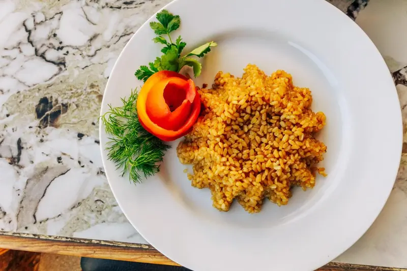 Assiette de riz doré décorée d'une tomate sculptée et d'herbes fraîches.