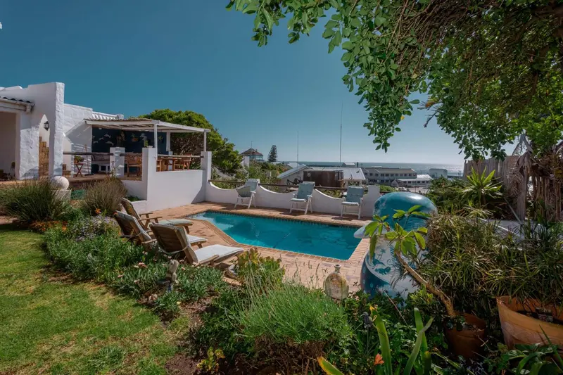 Une piscine bordée de chaises longues dans un jardin verdoyant.