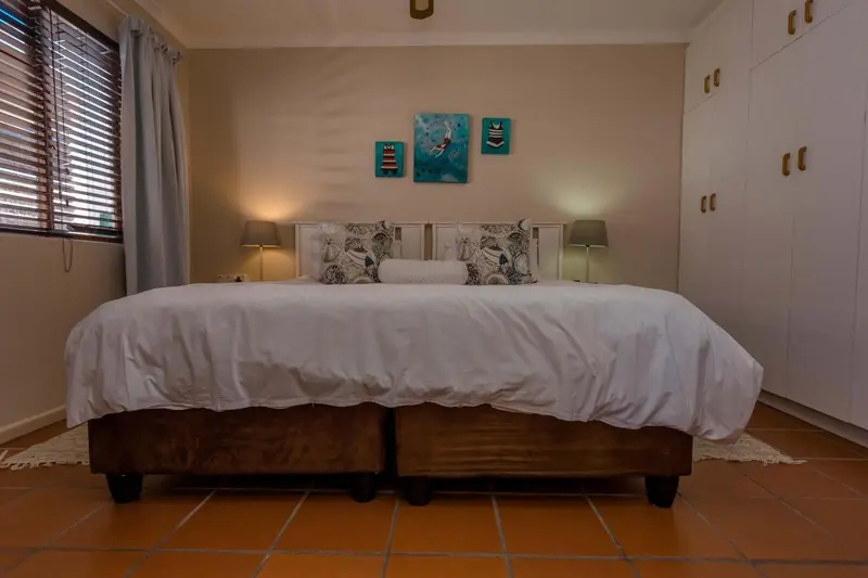 Une chambre lumineuse avec un grand lit recouvert d'une courtepointe blanche et de coussins.