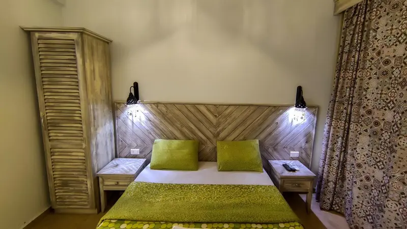 Une chambre lumineuse avec un lit recouvert d'une couette verte et des tables de chevet.