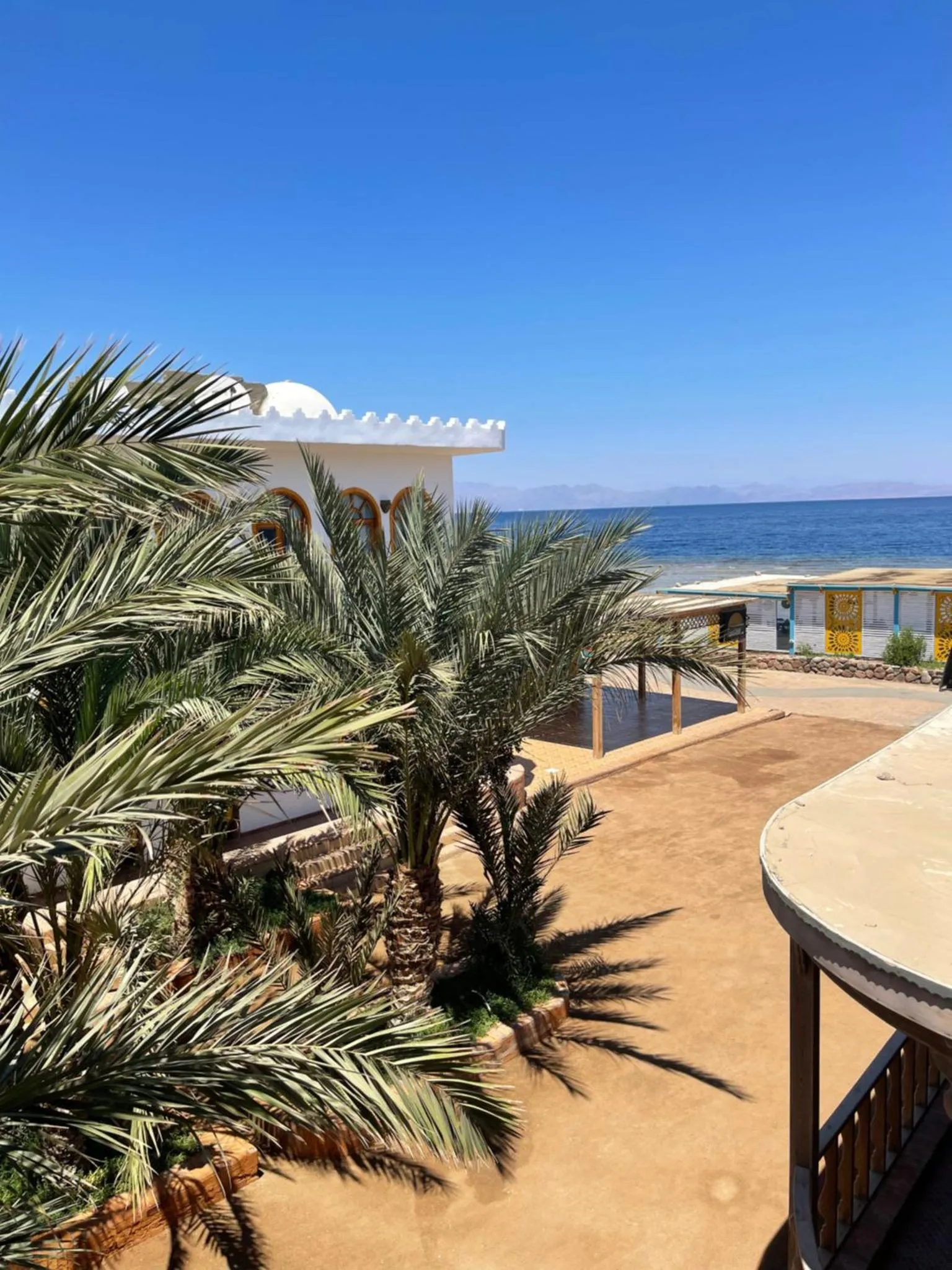 Terrasse ombragée avec végétation tropicale et vue sur la mer.