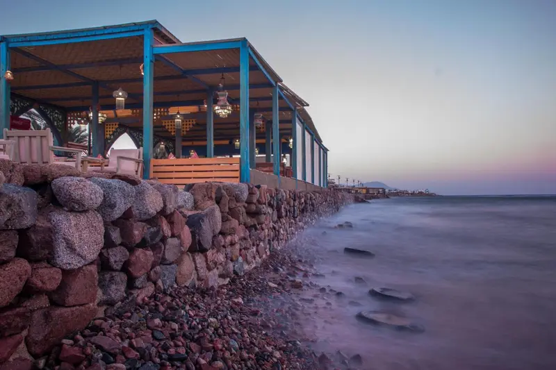 Terrasse ombragée avec mobilier en bord de mer au crépuscule.