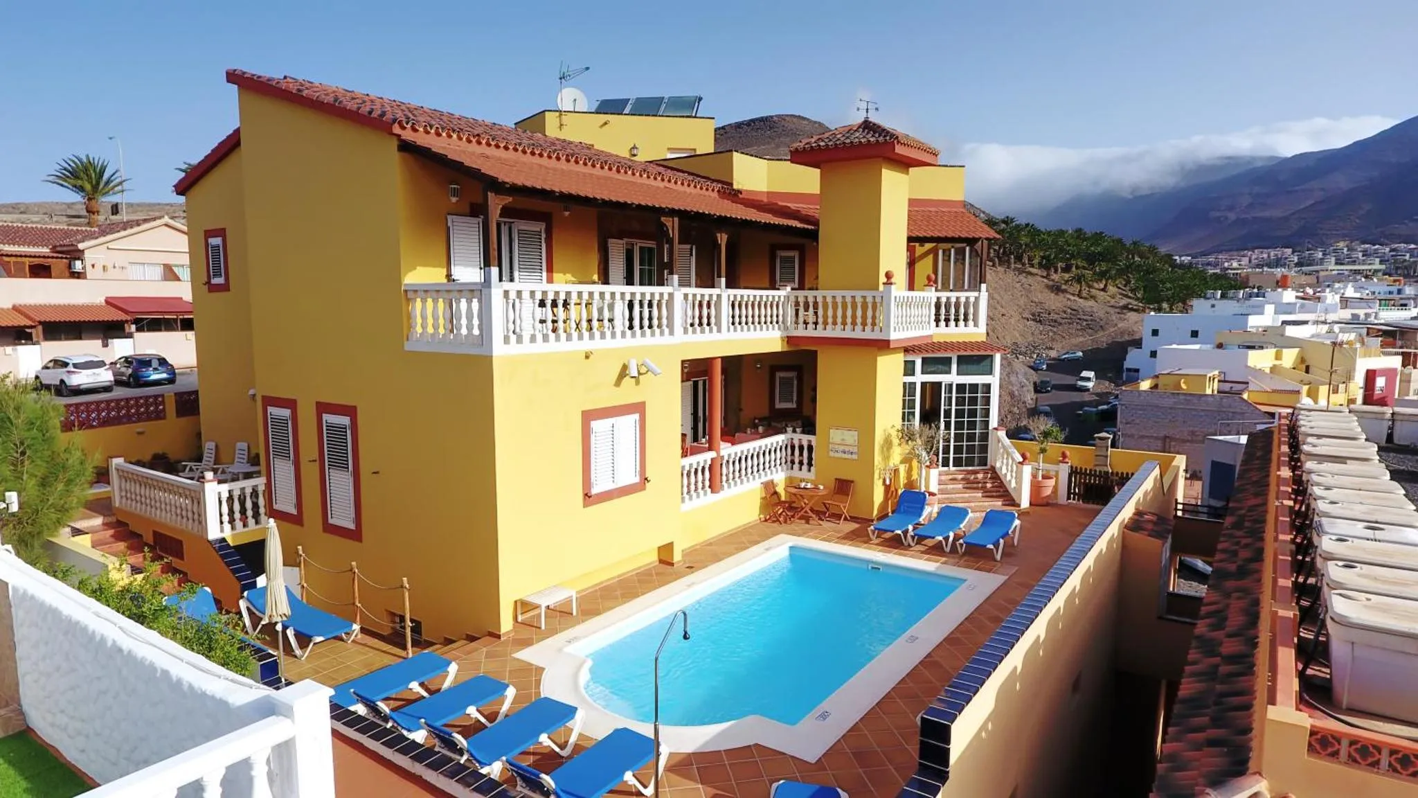 Bâtiment jaune à plusieurs niveaux avec piscine et transats bleus.