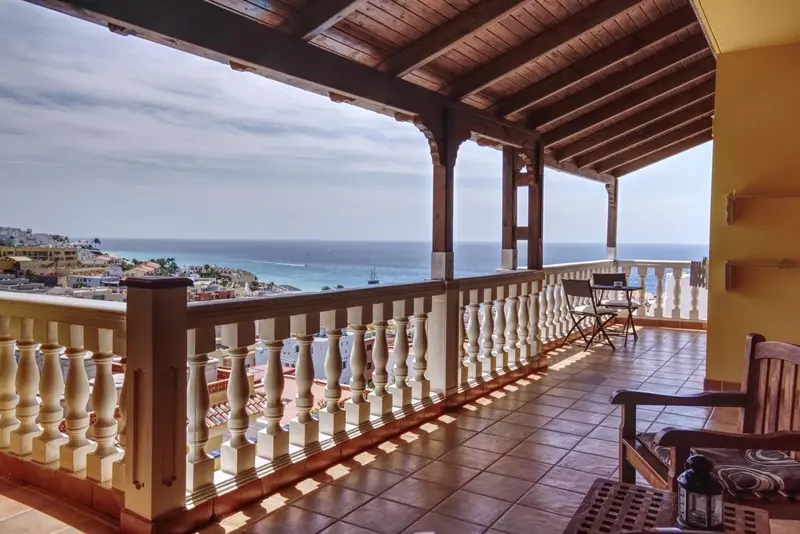 Terrasse carrelée avec mobilier en bois donnant sur une vue côtière.
