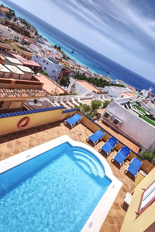 Vue aérienne d'une piscine et de transats sur un toit, avec la mer en arrière-plan.