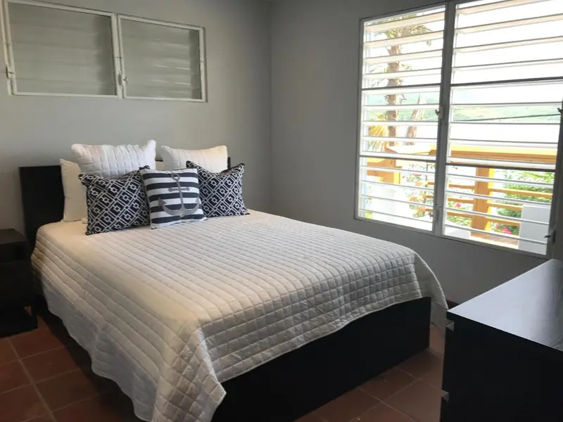 Une chambre lumineuse avec un grand lit recouvert d'une courtepointe blanche et de coussins.