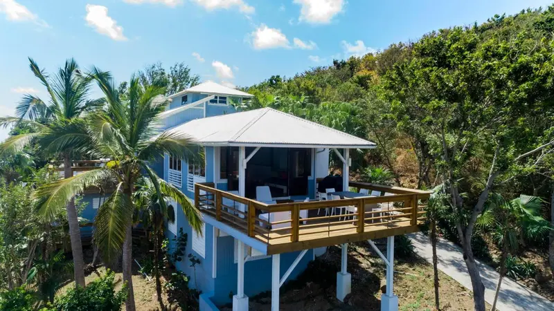 Vue aérienne d'une maison bleue avec une terrasse en bois et une végétation luxuriante.