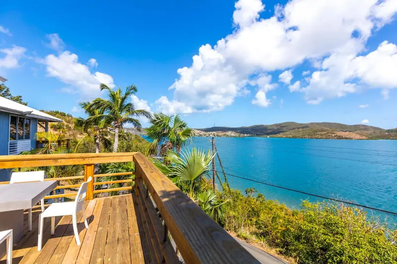 Terrasse en bois avec mobilier de jardin donnant sur une baie turquoise.