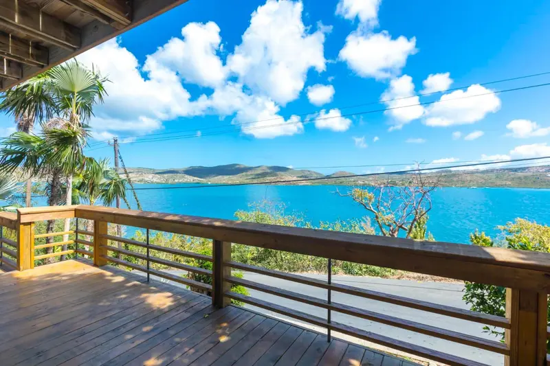 Terrasse en bois avec vue sur la mer et les collines verdoyantes sous un ciel nuageux.