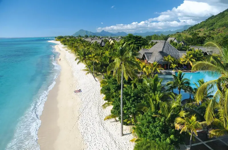 Vue aérienne d'une plage de sable blanc bordée de palmiers et de bungalows.