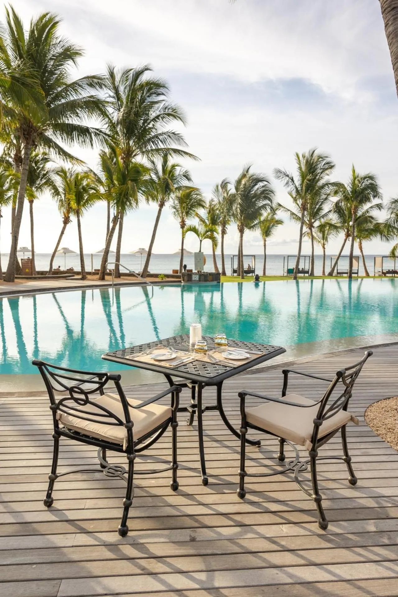 Une table est dressée au bord d'une piscine avec une vue sur la mer et des palmiers.
