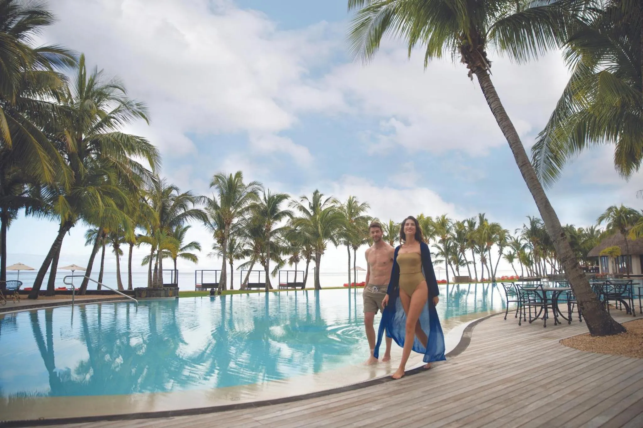 Un couple se promène le long d'une piscine bordée de palmiers.