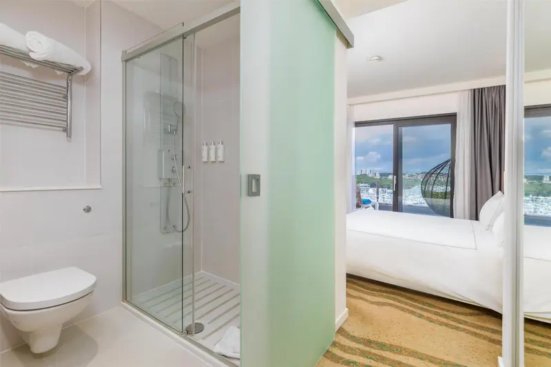 Une salle de bain moderne avec douche à l'italienne et toilettes, donnant sur une chambre lumineuse.
