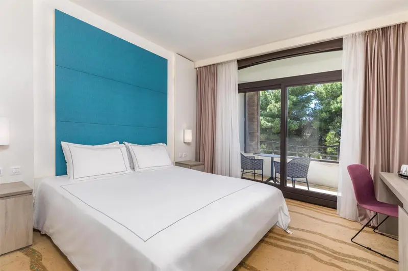 Une chambre lumineuse avec un grand lit et un accès à un balcon.
