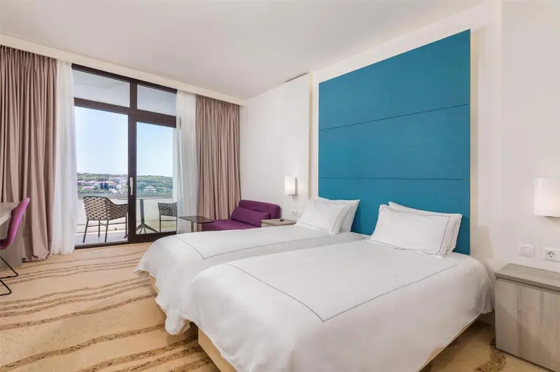 Une chambre lumineuse avec un grand lit et un balcon donnant sur la mer.