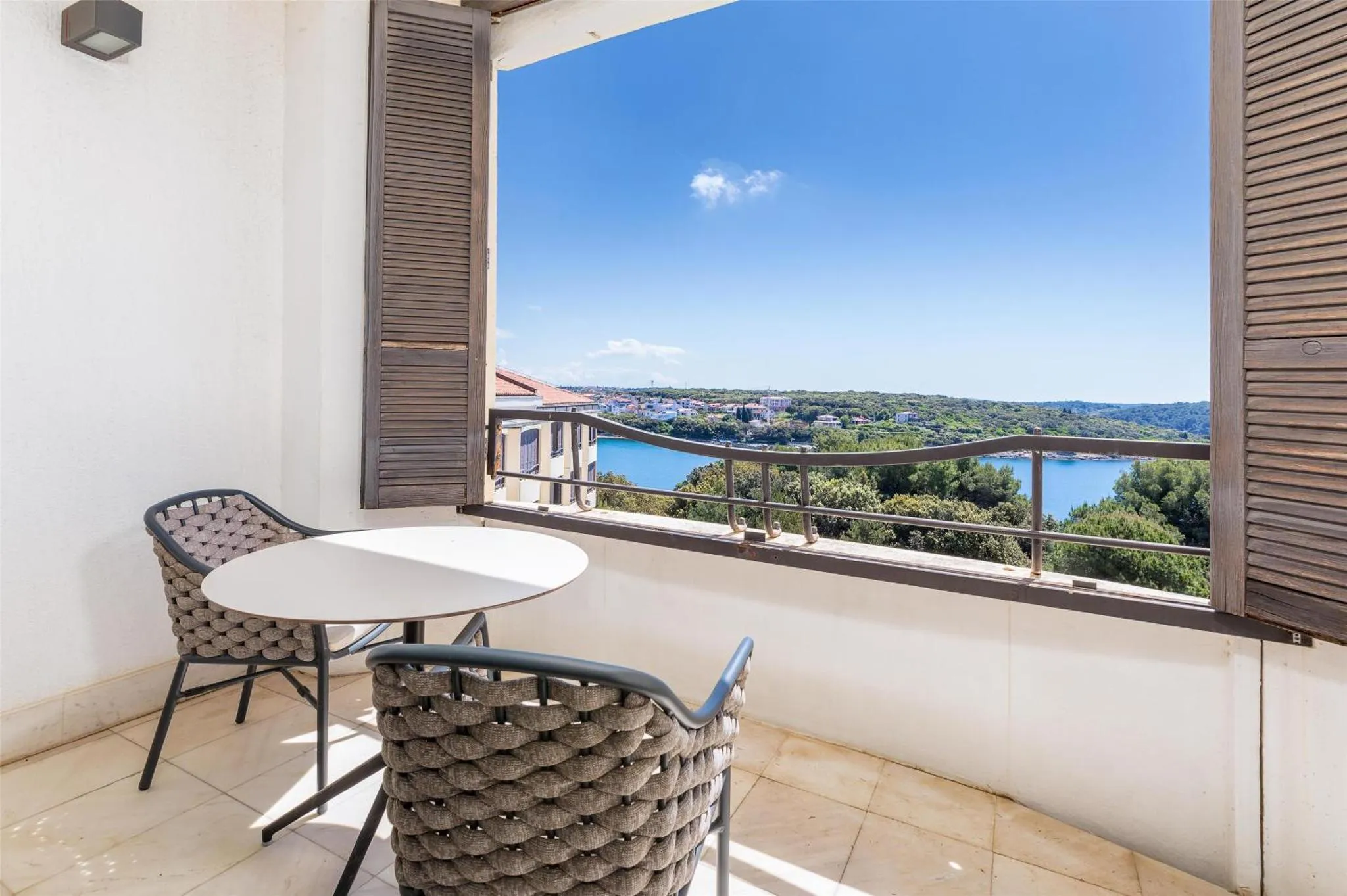 Une terrasse avec une table ronde et des chaises offre une vue sur la mer et la ville.