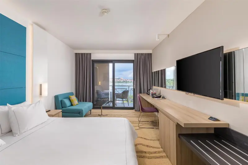 Une chambre lumineuse avec un lit, un bureau et un accès à un balcon.