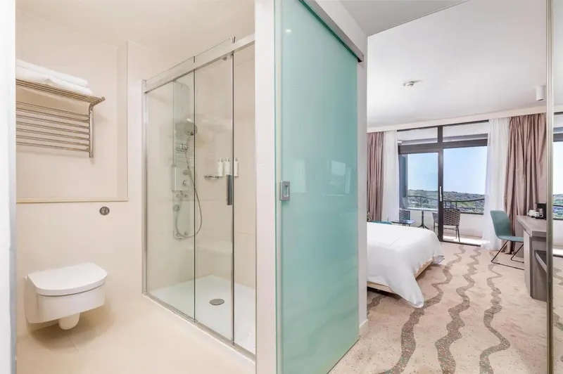 Une salle de bain moderne avec douche à l'italienne et accès à une chambre lumineuse.