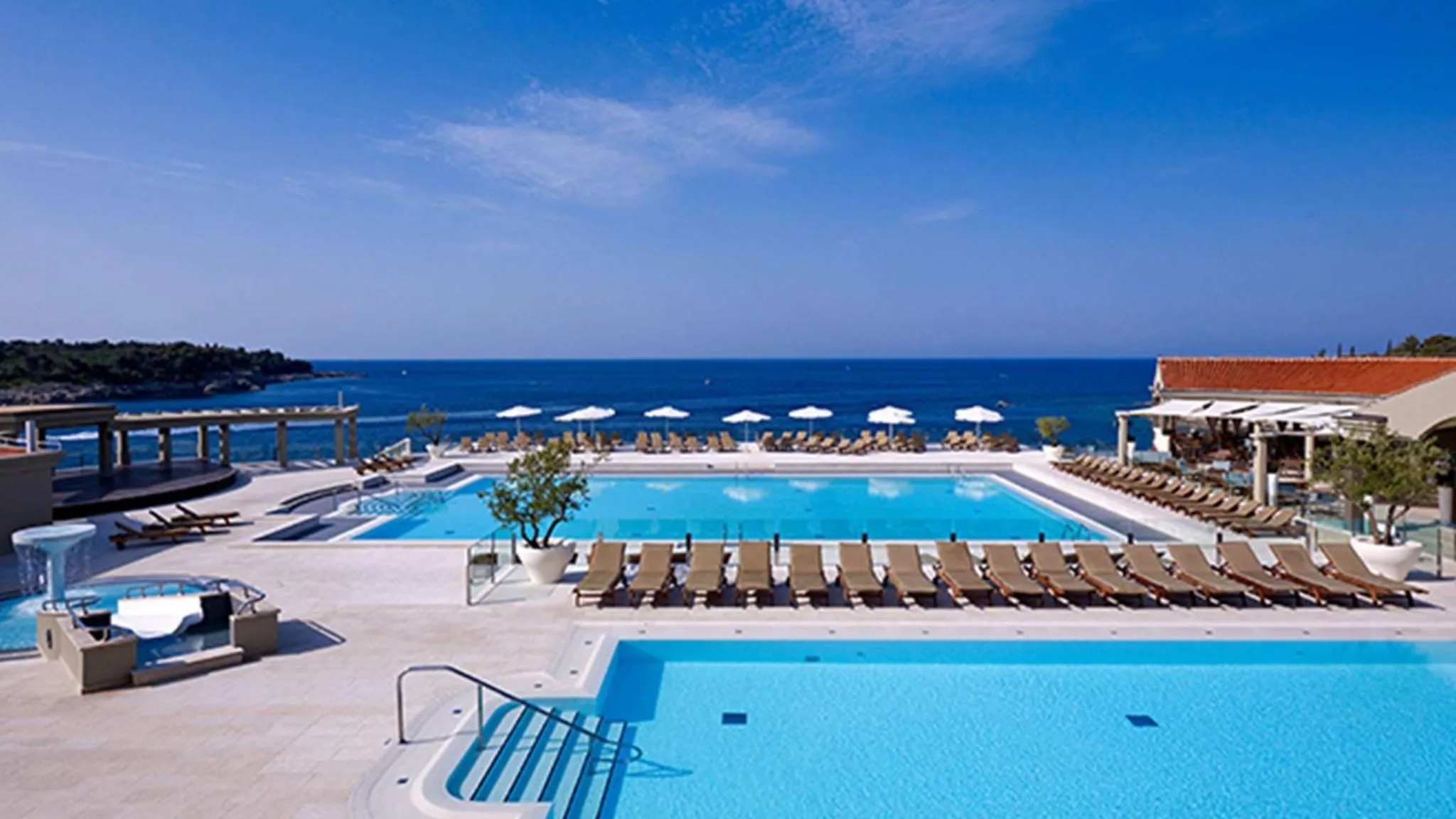 Piscine bleue bordée de transats avec vue sur la mer.