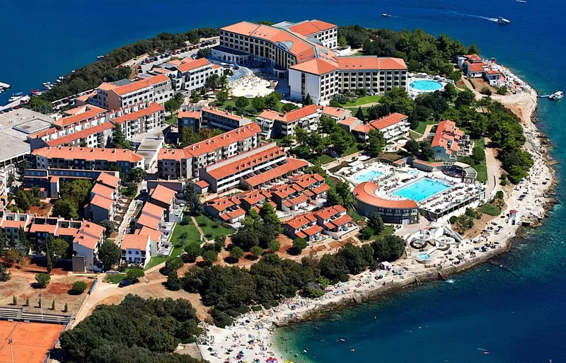 Vue aérienne d'un complexe hôtelier en bord de mer avec des piscines et des plages.