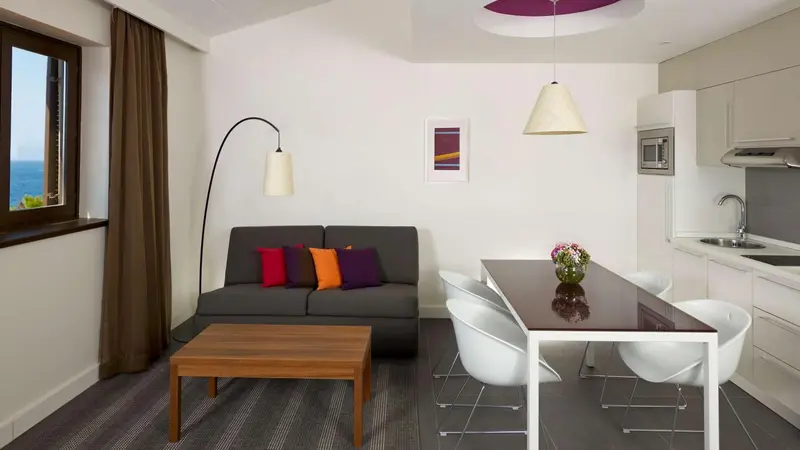Espace de vie lumineux avec canapé, table à manger et cuisine équipée.
