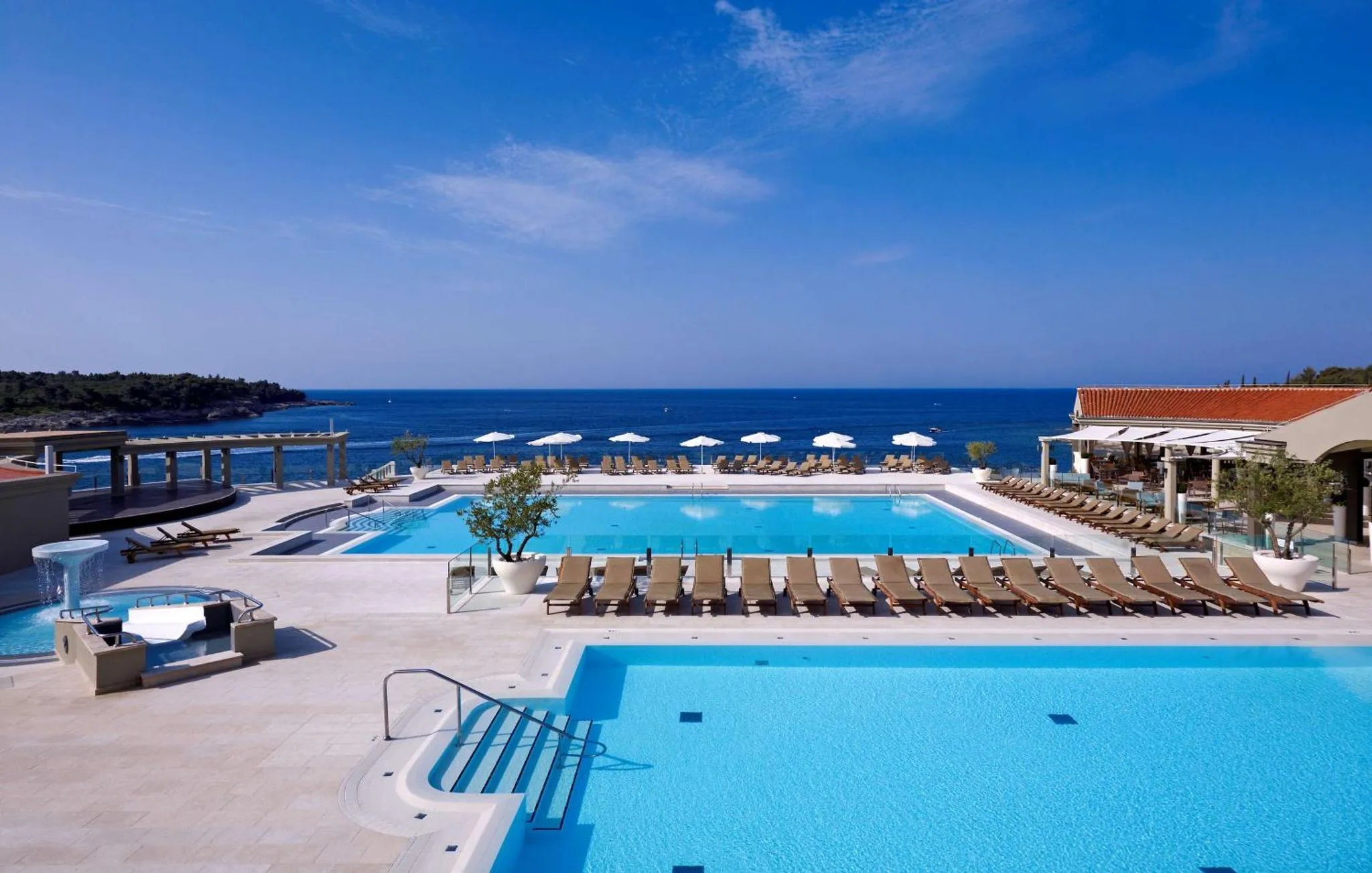 Piscine bleue bordée de transats avec vue sur la mer et le ciel bleu.