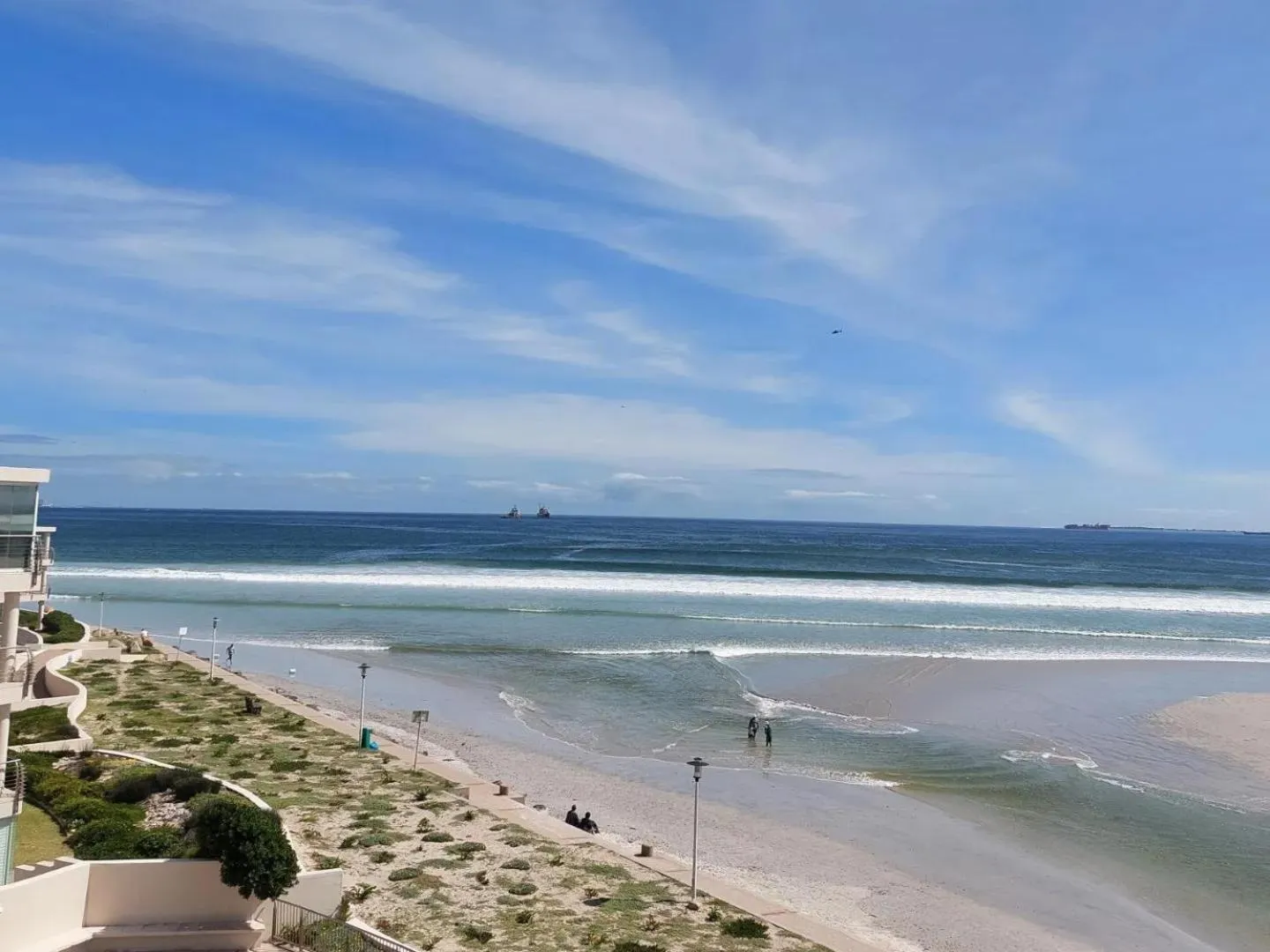 Vue d'une plage de sable fin avec des vagues et quelques personnes.
