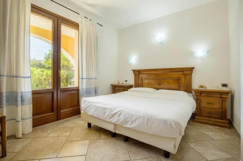 Une chambre lumineuse avec un grand lit et une fenêtre ouverte sur la végétation.